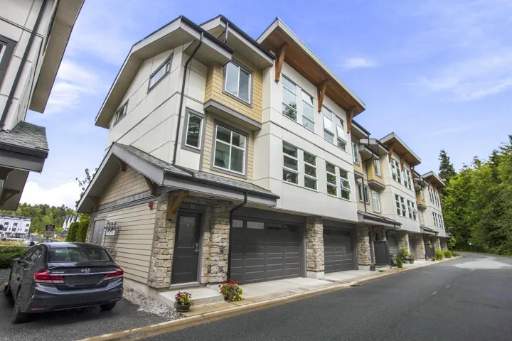 Modern multi-story facade featuring light siding, stone accents, and dark garage doors