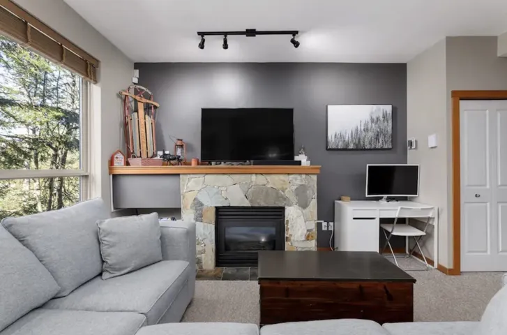 Carpeted living area with track lighting, a stone fireplace, and a desk