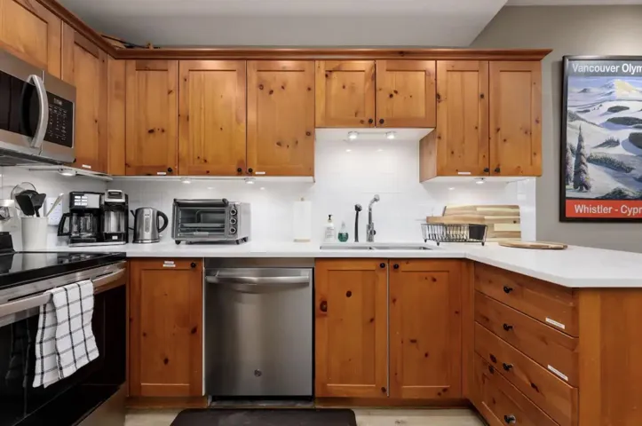 Kitchen featuring stainless steel appliances, light countertops, decorative backsplash, and brown cabinets