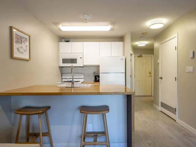 Kitchen featuring white cabinetry, a peninsula, white appliances, a breakfast bar, and light wood-type flooring