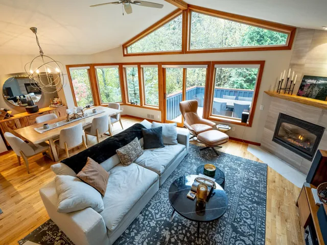 Living room with light wood-style floors, a fireplace, a chandelier, a ceiling fan, and high vaulted ceiling