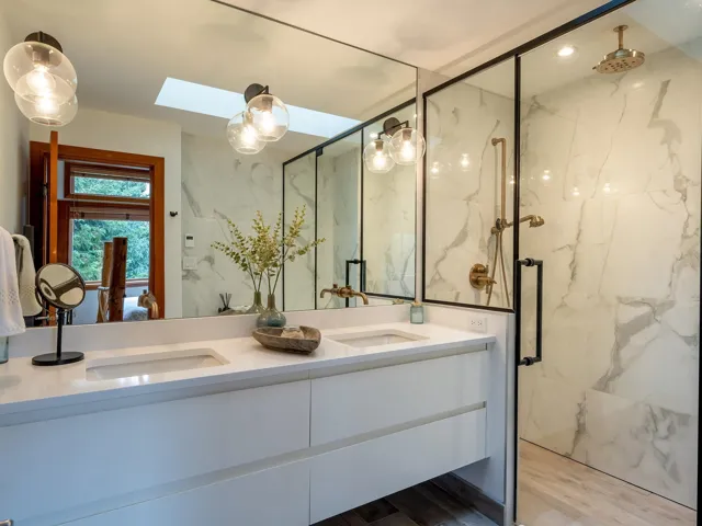 Bathroom with a skylight, double vanity, dark wood finished floors, a marble finish shower, and tile walls