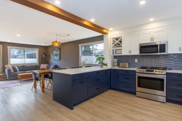 Kitchen featuring white cabinets, open floor plan, stainless steel appliances, light countertops, and beam ceiling