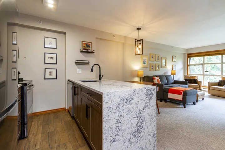 Kitchen featuring a sink, stainless steel appliances, a peninsula, light stone counters, and hanging light fixtures
