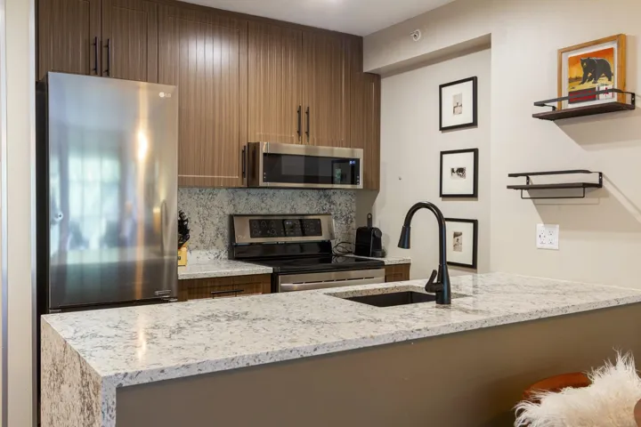 Kitchen featuring stainless steel appliances, a sink, backsplash, light stone countertops, and open shelves