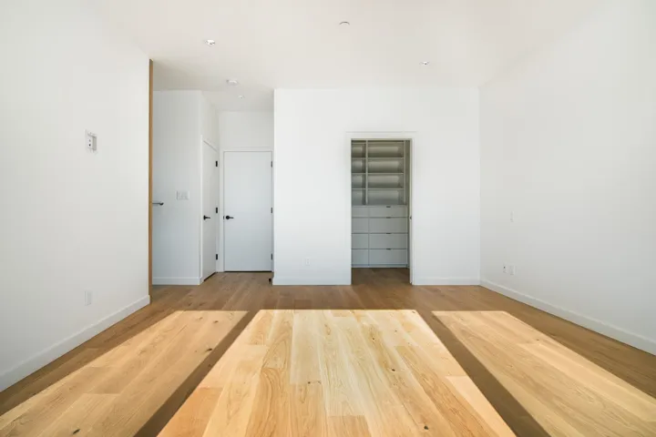 Unfurnished bedroom featuring baseboards, wood finished floors, a walk in closet, and a closet