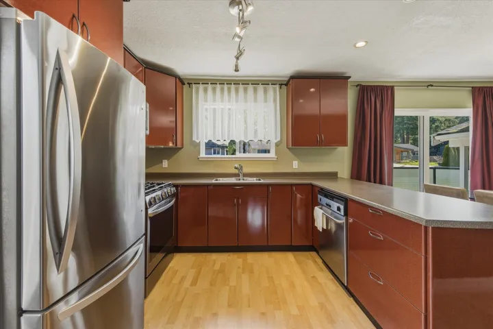 Kitchen with stainless steel appliances, a peninsula, a textured ceiling, dark countertops, and light wood-type flooring