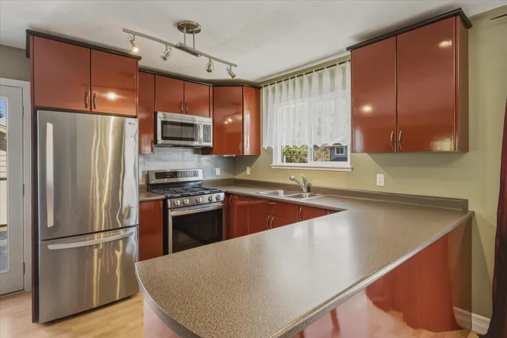 Kitchen featuring stainless steel appliances, a peninsula, light wood finished floors, rail lighting, and a breakfast bar