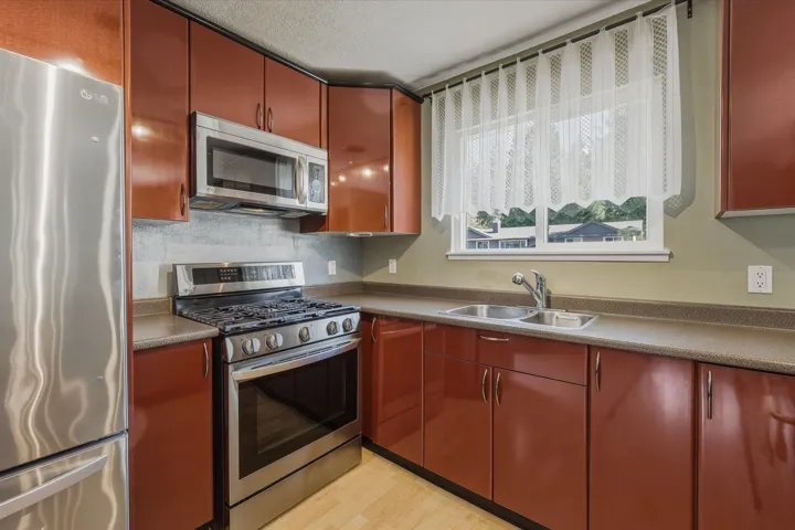Kitchen with stainless steel appliances, light wood finished floors, a textured ceiling, and dark countertops