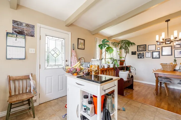 Kitchen featuring hanging light fixtures, an inviting chandelier, dark countertops, lofted ceiling with beams, and baseboards