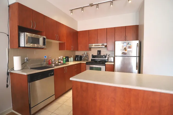 Kitchen with stainless steel appliances, tasteful backsplash, light countertops, light tile patterned floors, and under cabinet range hood