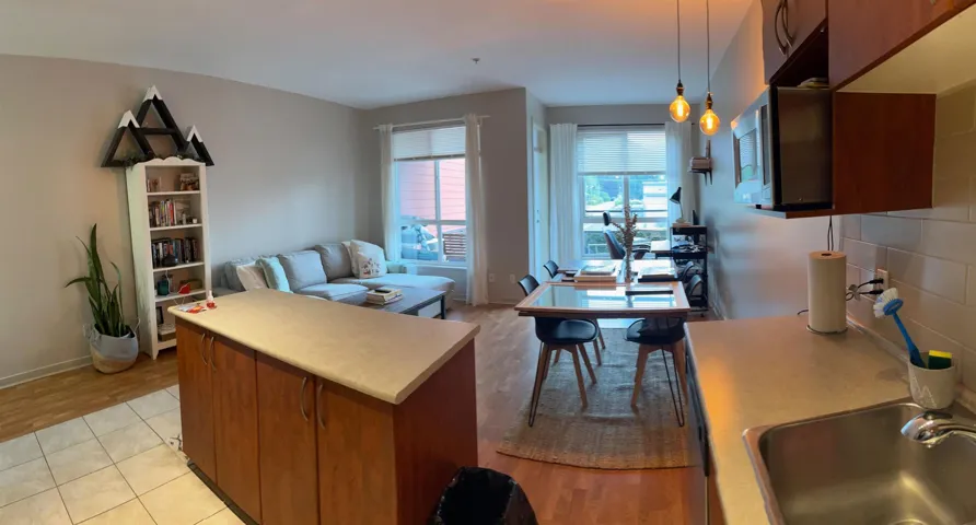 Kitchen with brown cabinetry, light countertops, hanging light fixtures, open floor plan, and light wood finished floors