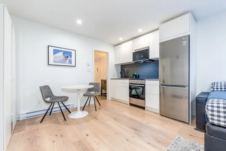 Kitchen featuring stainless steel appliances, a baseboard heating unit, tasteful backsplash, light wood-style floors, and white cabinetry