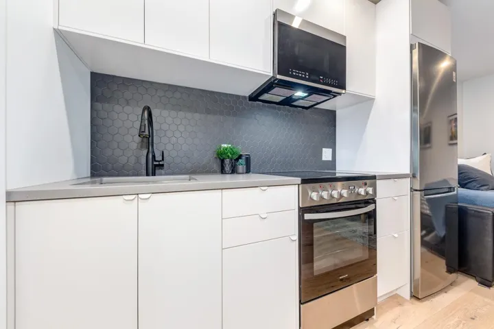 Kitchen featuring stainless steel appliances, tasteful backsplash, white cabinetry, modern cabinets, and light wood-type flooring