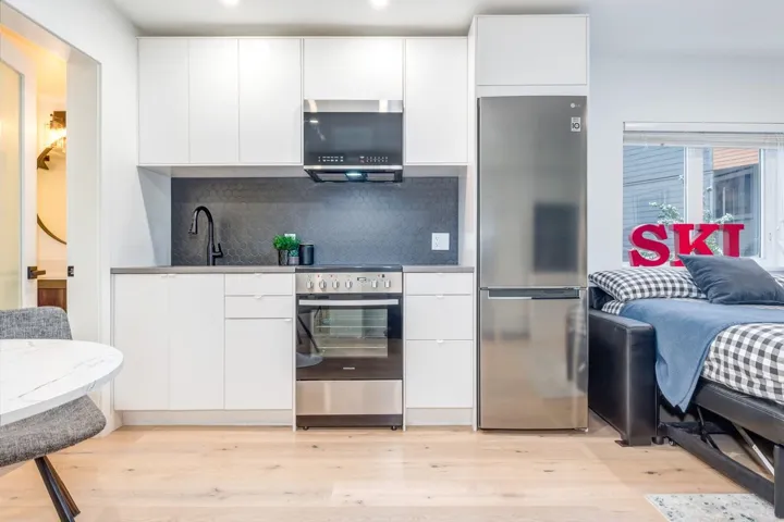 Kitchen with modern cabinets, backsplash, stainless steel appliances, white cabinetry, and light wood finished floors