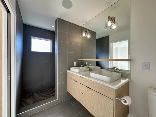 Full bathroom with tiled shower, double vanity, a sink, tile patterned floors, and toilet