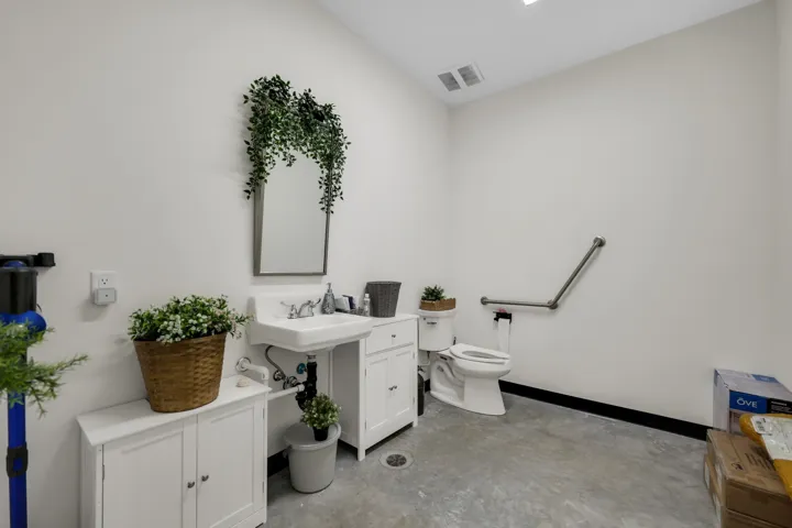 Powder room featuring a wall-mounted sink with chrome fixtures, a white toilet with a grab bar, concrete flooring, and recessed lighting