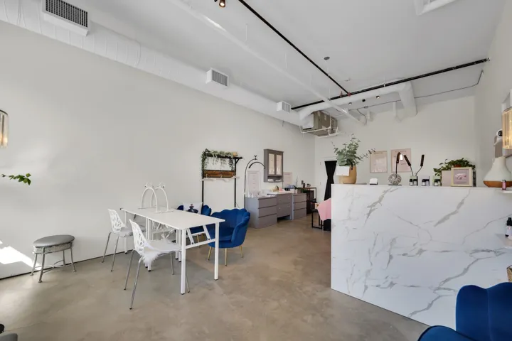 Spacious interior featuring concrete flooring, white walls, exposed ductwork, track lighting, and a white marble-patterned reception counter