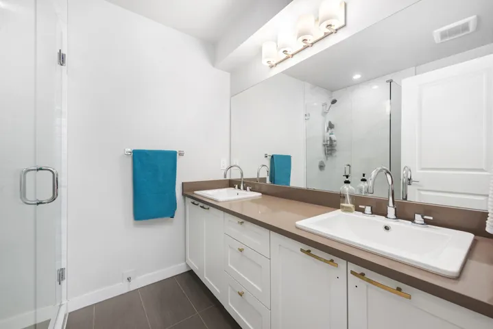 Bathroom with dark tile patterned flooring, a shower stall, and double vanity