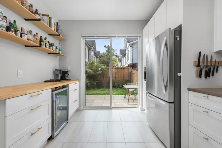 Indoor dry bar with freestanding refrigerator, white cabinets, beverage cooler, light tile patterned floors, and butcher block counters