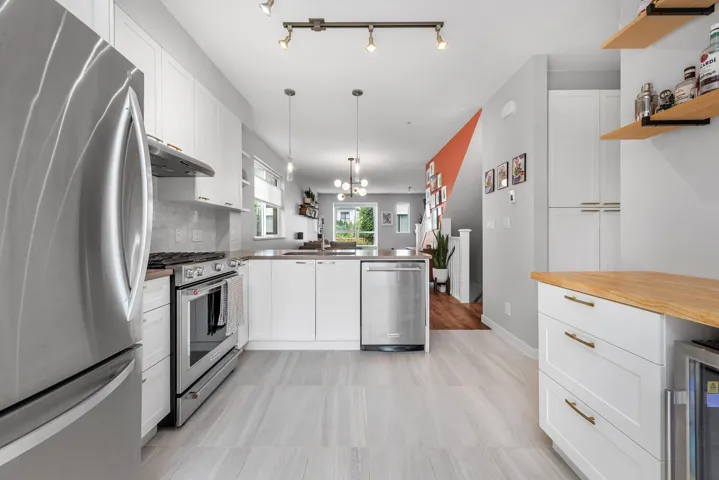 Kitchen with white cabinetry, appliances with stainless steel finishes, a peninsula, decorative light fixtures, and extractor fan