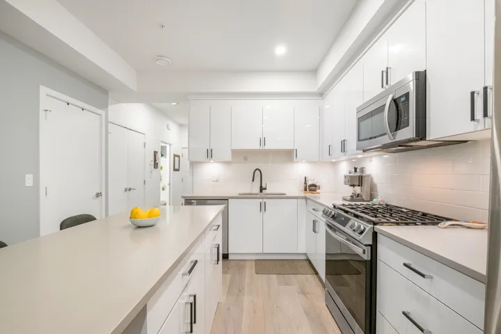 Kitchen with stainless steel appliances, a sink, light wood finished floors, light countertops, and white cabinetry