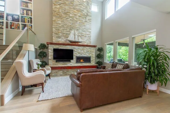 Living area with baseboards, wood finished floors, a wealth of natural light, and a stone fireplace
