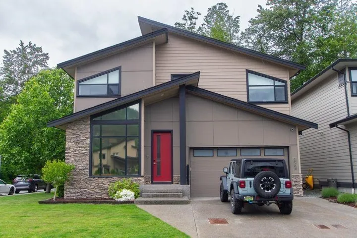 Contemporary house with a garage, stone siding, a front yard, and driveway