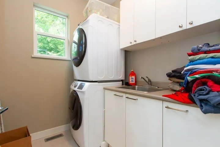 Clothes washing area featuring light tile patterned floors, a sink, visible vents, stacked washing maching and dryer, and cabinet space