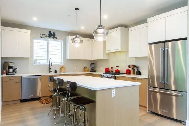 Kitchen with a breakfast bar, a sink, appliances with stainless steel finishes, light wood-type flooring, and custom range hood