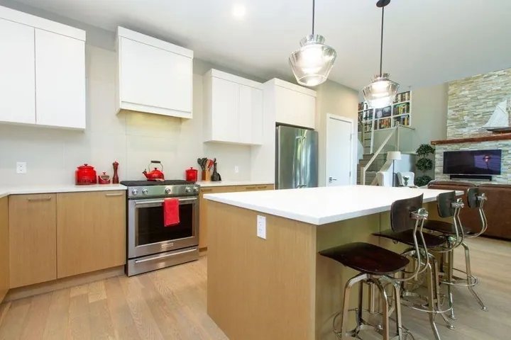 Kitchen with stainless steel appliances, light wood finished floors, light countertops, and a kitchen breakfast bar