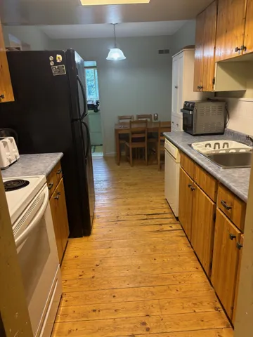Kitchen featuring brown cabinetry, white appliances, light wood-style floors, decorative light fixtures, and decorative backsplash
