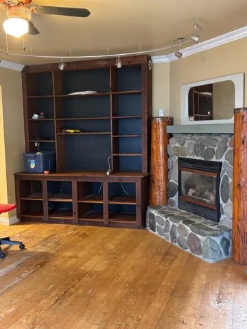 Living room featuring crown molding, hardwood / wood-style flooring, and a stone fireplace