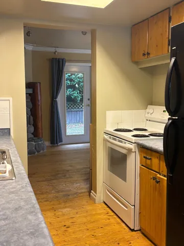Kitchen with brown cabinets, electric stove, light wood-style flooring, and freestanding refrigerator