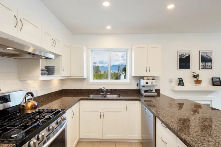 Kitchen with white cabinetry, under cabinet range hood, dark stone counters, appliances with stainless steel finishes, and a sink