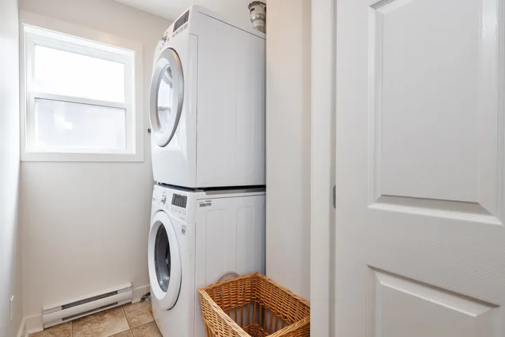 Clothes washing area featuring stacked washer / drying machine, a baseboard radiator, laundry area, and baseboards