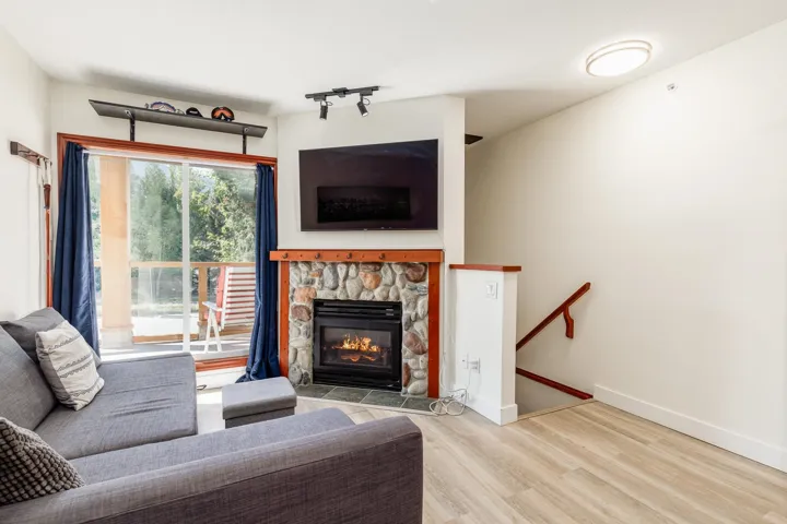 Stone-clad fireplace with a gas insert, sliding glass door with exterior access, light wood-finish flooring, and a built-in shelf