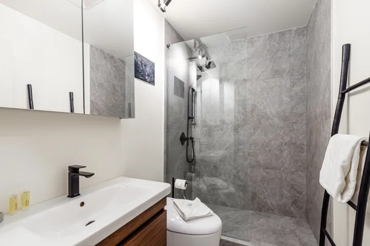 Walk-in shower with full-height stone-look tile, glass enclosure, and matte black fixtures