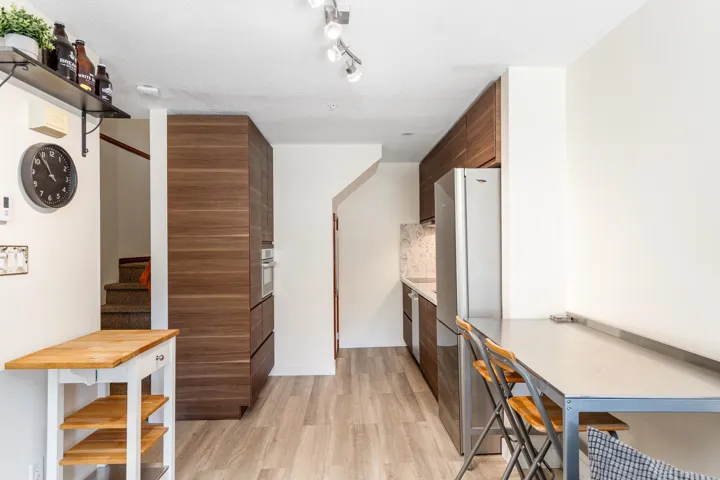 Compact kitchen featuring wood-finish cabinetry, stainless steel appliances, a tiled backsplash, and light wood-finish flooring