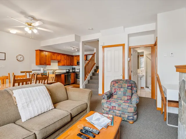 Living area featuring light colored carpet, a fireplace, a ceiling fan, baseboards, and stairway