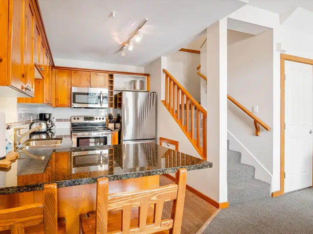 Kitchen featuring brown cabinetry, decorative backsplash, appliances with stainless steel finishes, open shelves, and a sink