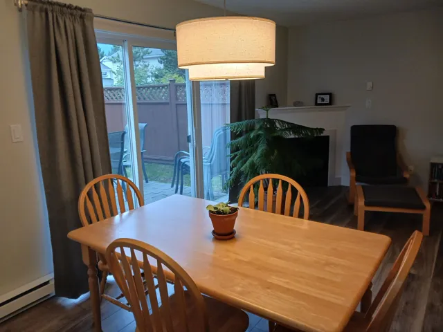 Dining area featuring wood-finish flooring, a tiered drum pendant light fixture, a fireplace with a white mantel, and sliding glass doors with access to an exterior patio