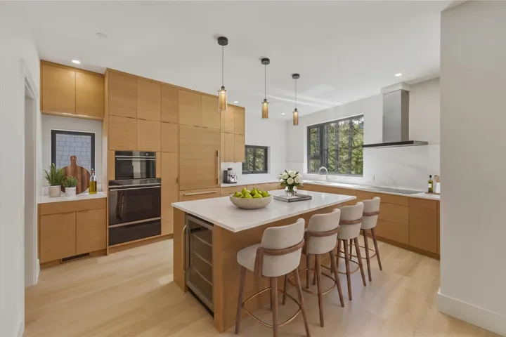 Contemporary kitchen featuring light wood-finish cabinetry, white stone countertops, a built-in cooktop, and a stainless steel range hood