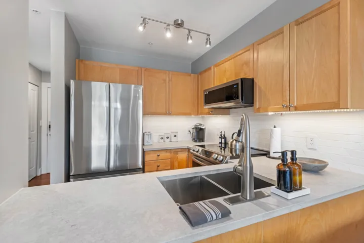Kitchen featuring light countertops, decorative backsplash, appliances with stainless steel finishes, and light brown cabinets
