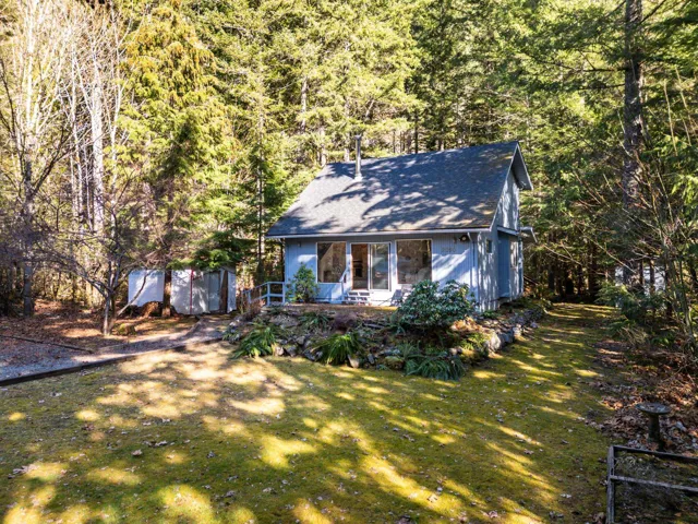 View of front of property with roof with shingles, an outbuilding, a wooded view, and a front yard