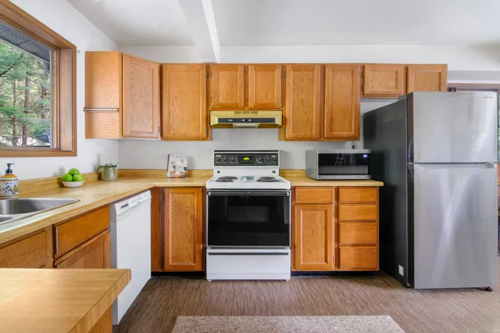 Kitchen with light countertops, appliances with stainless steel finishes, dark wood-type flooring, beamed ceiling, and under cabinet range hood