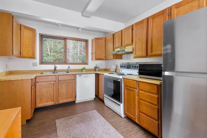 Kitchen featuring dark wood finished floors, light countertops, appliances with stainless steel finishes, a sink, and under cabinet range hood