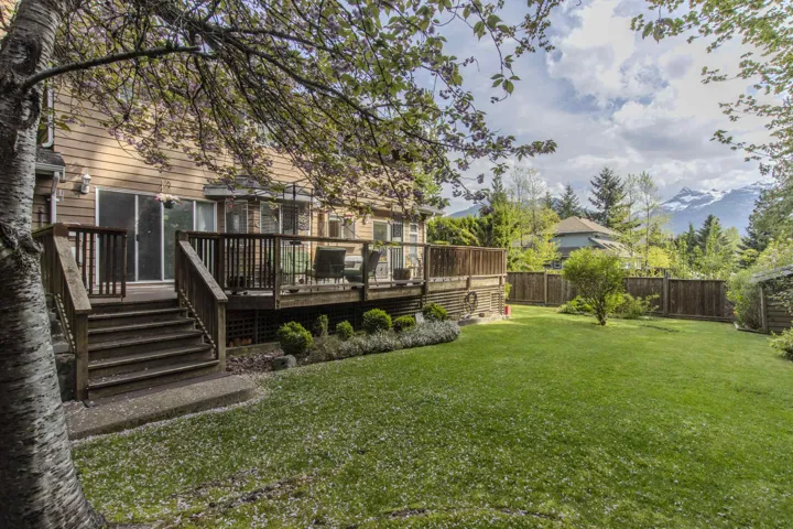Expansive backyard featuring a large wooden deck with stairs to the lawn, mature trees, and a wooden fence boundary