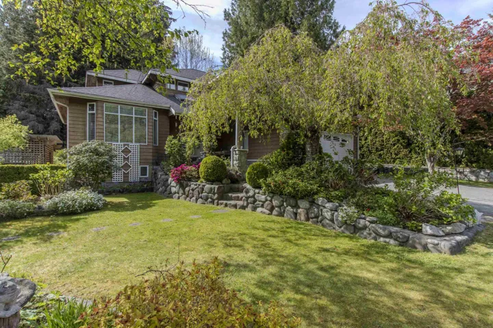 Landscaped front yard featuring a manicured lawn, stone retaining walls, and mature plantings