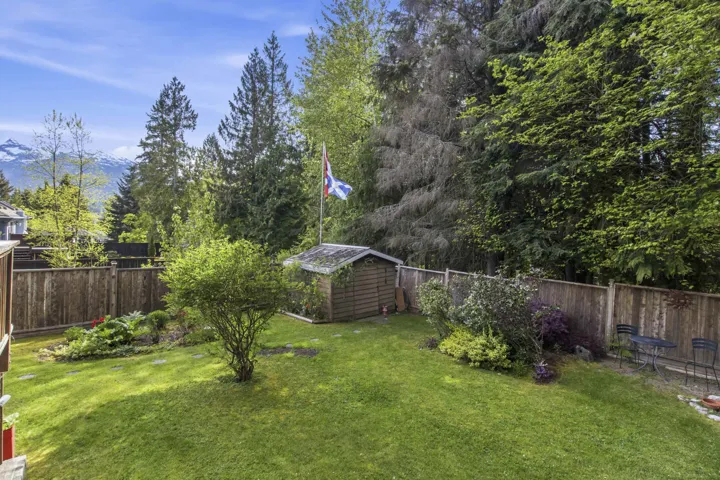 Expansive, fenced backyard featuring a grassy lawn, established garden beds, a storage shed, and a mountain backdrop